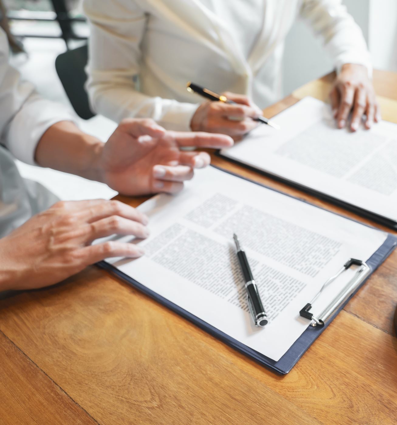 Two people reviewing legal documents with pens and clipboards on a wooden table, symbolizing negotiations for asset division.