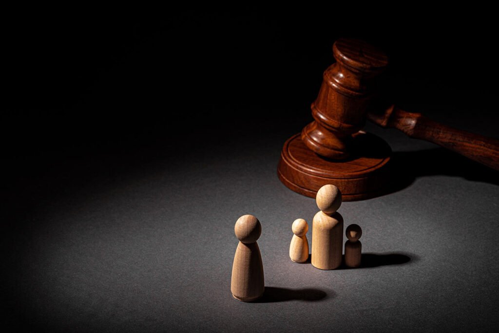 Wooden figurines representing a family and a judge's gavel on a dark background, symbolising family law and court proceedings.