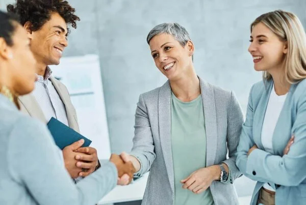 Group of diverse business professionals, including employment lawyers, smiling and shaking hands during a meeting in an office setting.