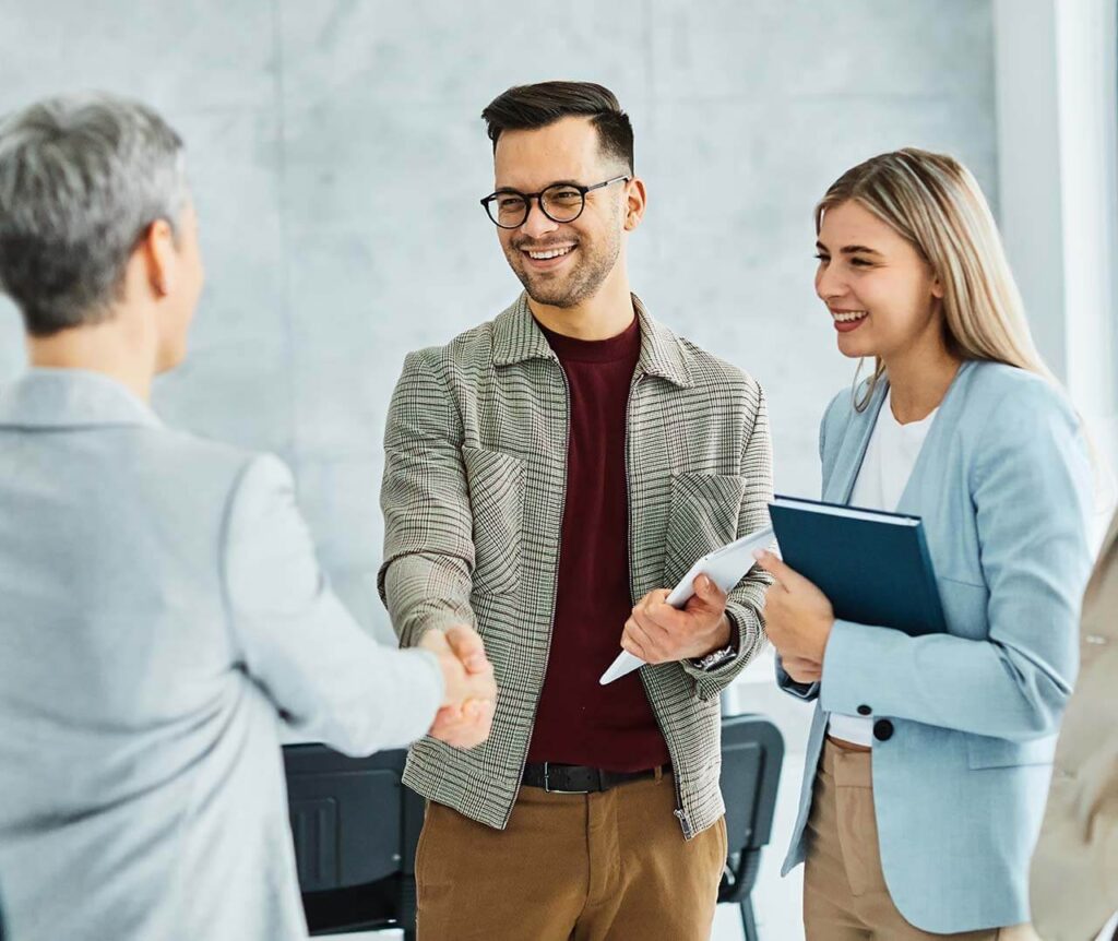 Two employment lawyers, a male and a female, smiling and shaking hands with a client in an office setting.