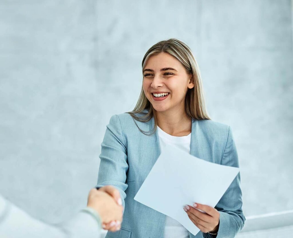 Female employment lawyer smiling and shaking hands with a client while holding legal documents in an office setting.