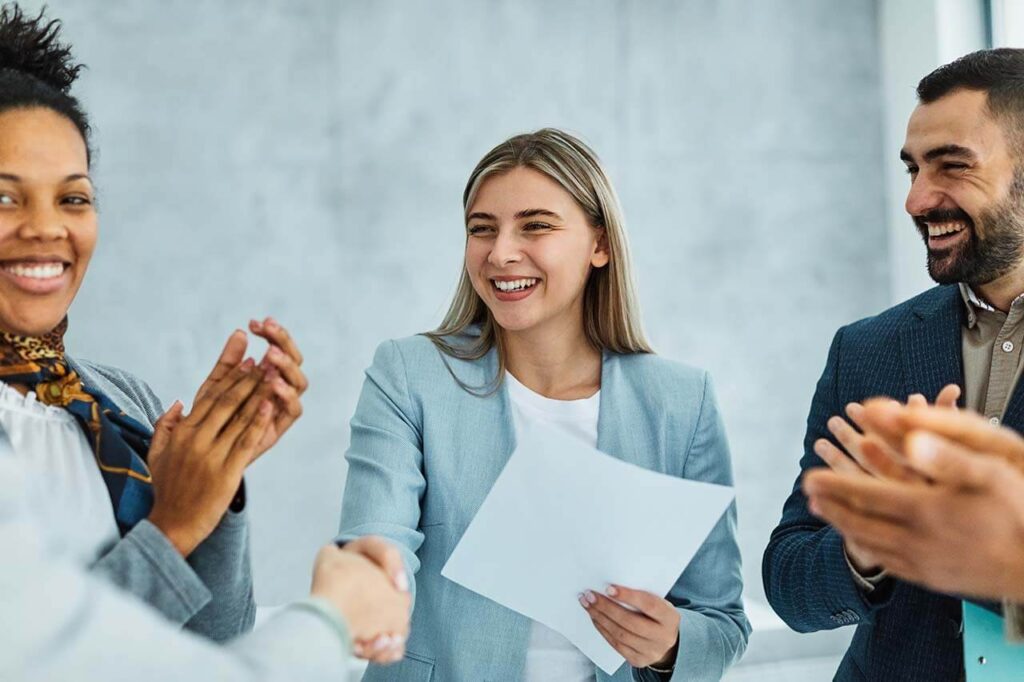 Group of diverse business professionals, including an employment lawyer, smiling and clapping hands in an office setting after a successful consultation.